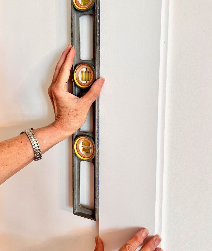 a woman's hand hold a long level against a piece of shiplap on a wall