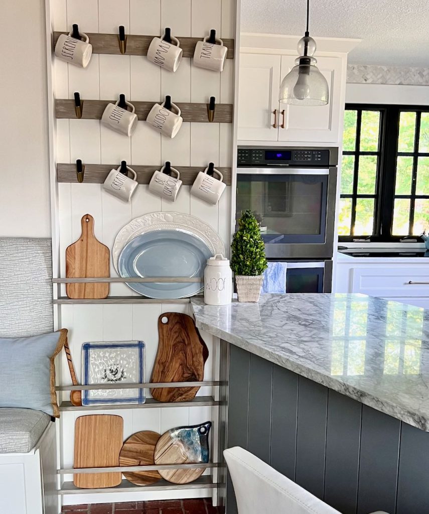 The kitchen side of the banquette is shown with. mugs hanging from hooks on strips of wood over thin plate racks