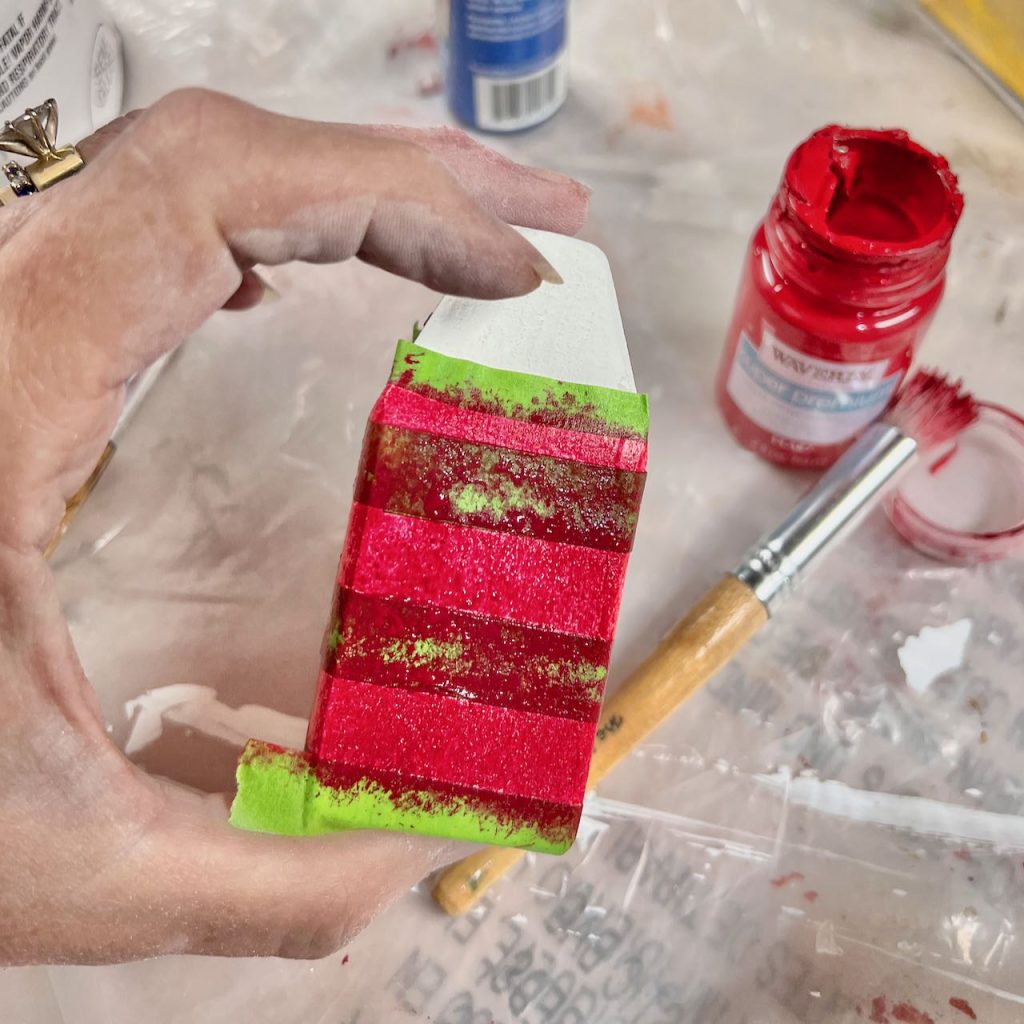 painters tape wraps a small wooden buoy and red paint stenciled on