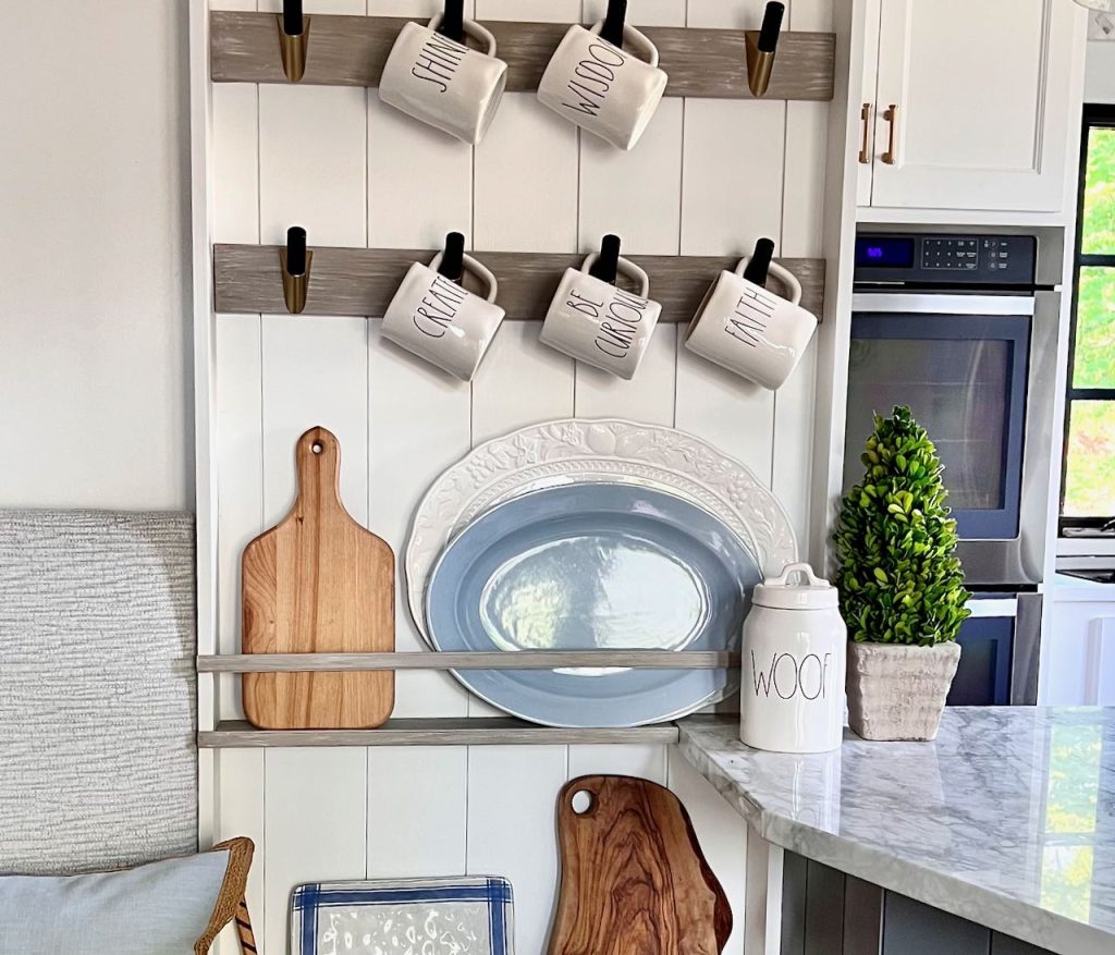 mugs hanging on the bottom two rows of a mug rack above a cutting board and platters on the top shelf of a plate rack