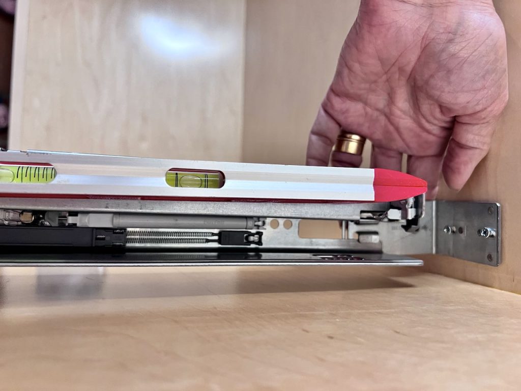 hand is placing a level on drawer rail inside a cabinet frame