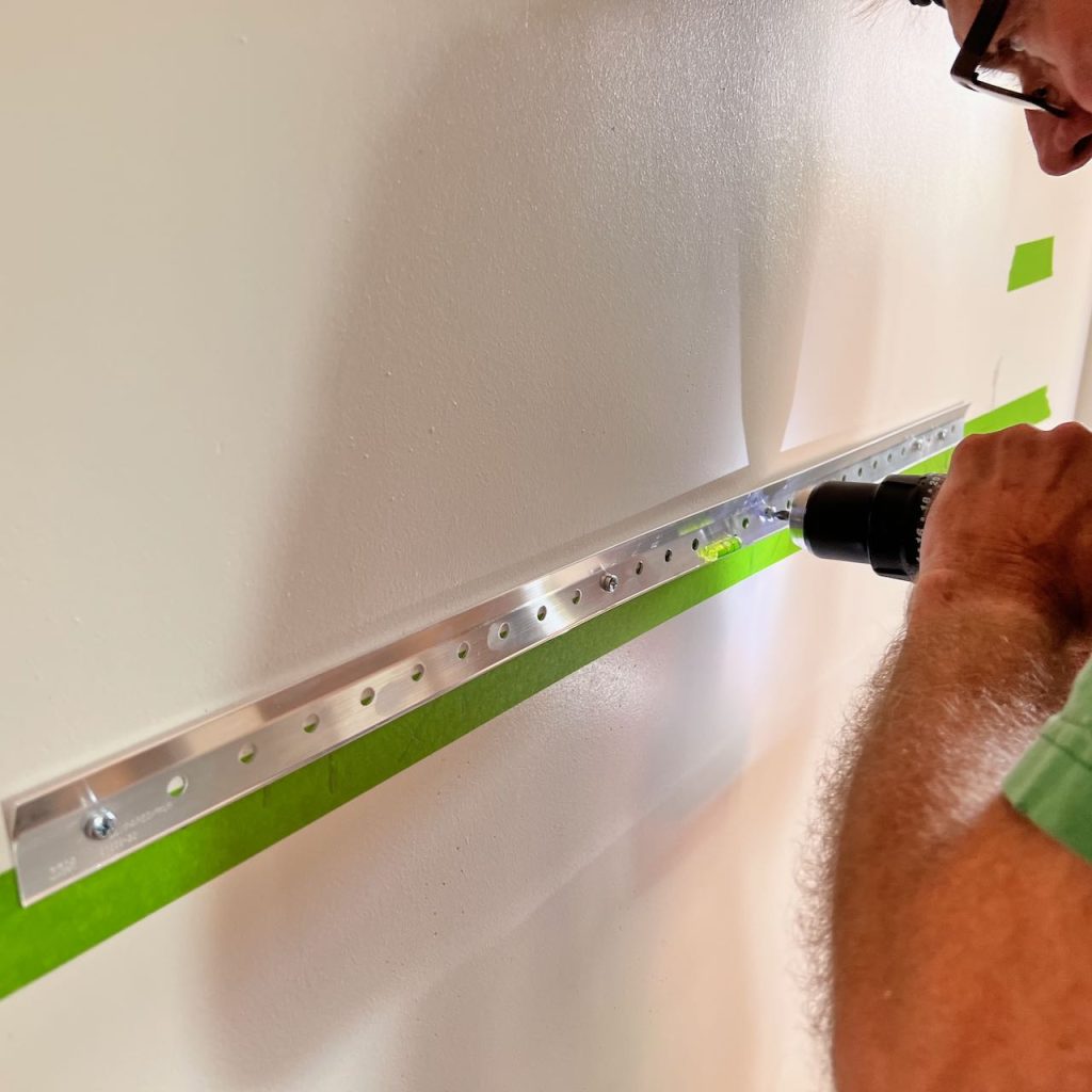 man installing a french cleat with screws iin the wall