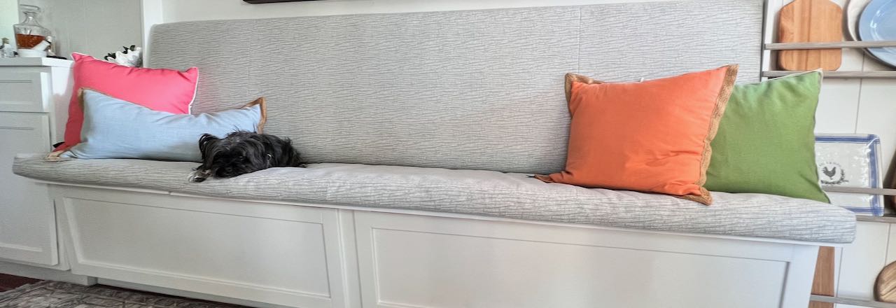 wide closeup shot of a small dog and two throw pillows are on the cushioned seat of a built-in banquette