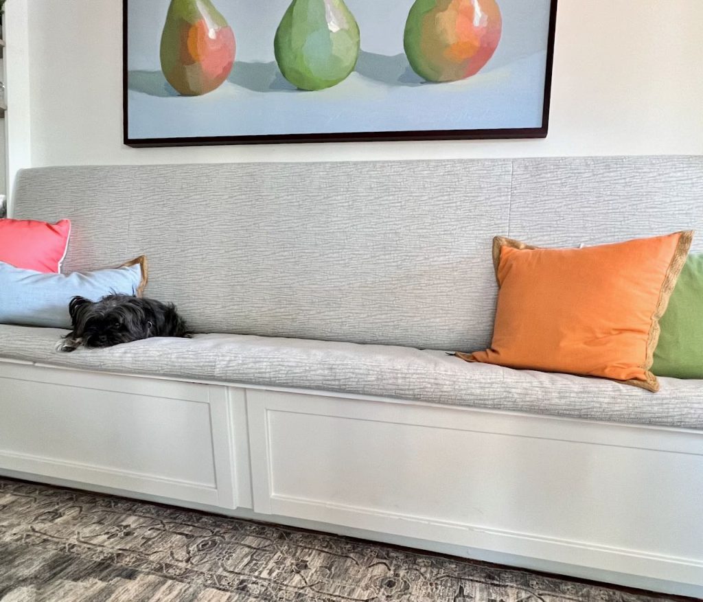 a small dog and two throw pillows are on the cushioned seat of a built-in banquette