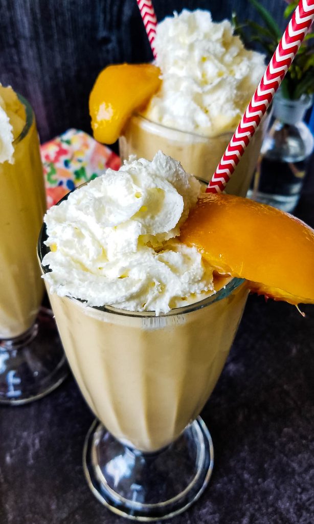 peach milkshakes with whipped cream and a peach slice for garnish
