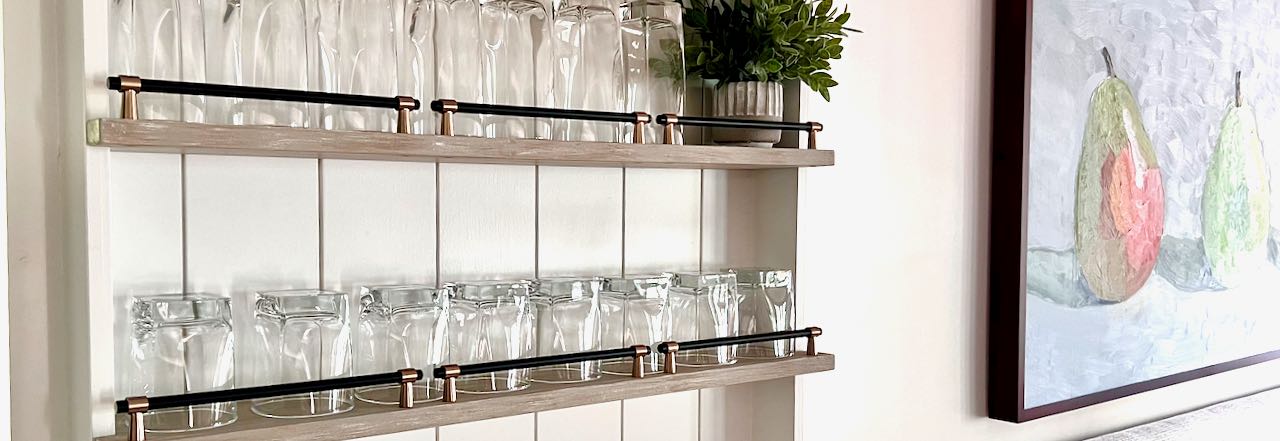 loseup of bar glassware on narrow open shelves with railings on a shiplap backing