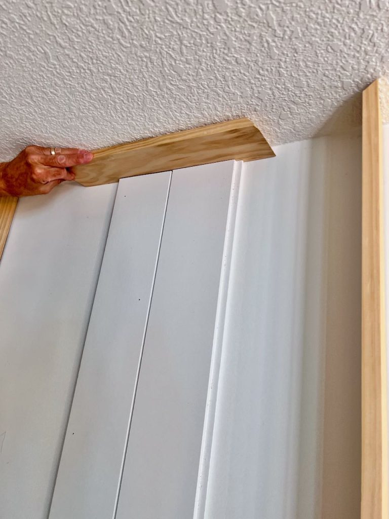 a man's hand is holding a piece of scrap wood between shiplap planks and the ceiling