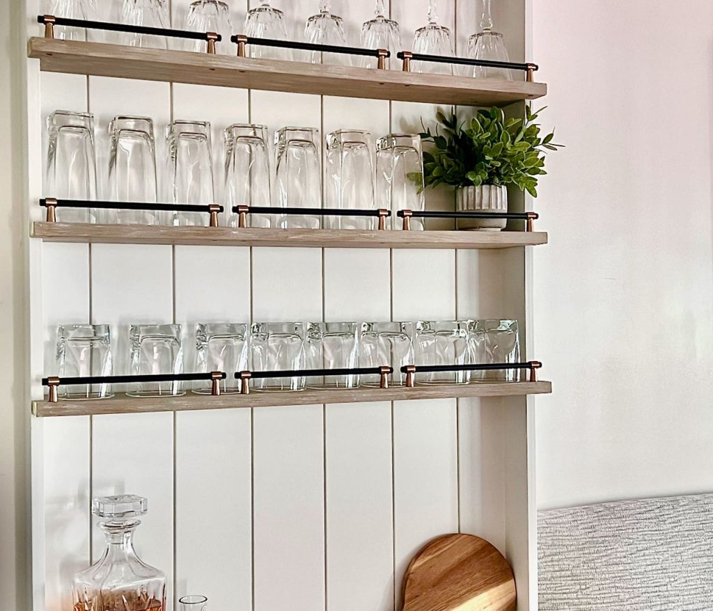 closeup of bar glassware on narrow open shelves with railings on a shiplap backing