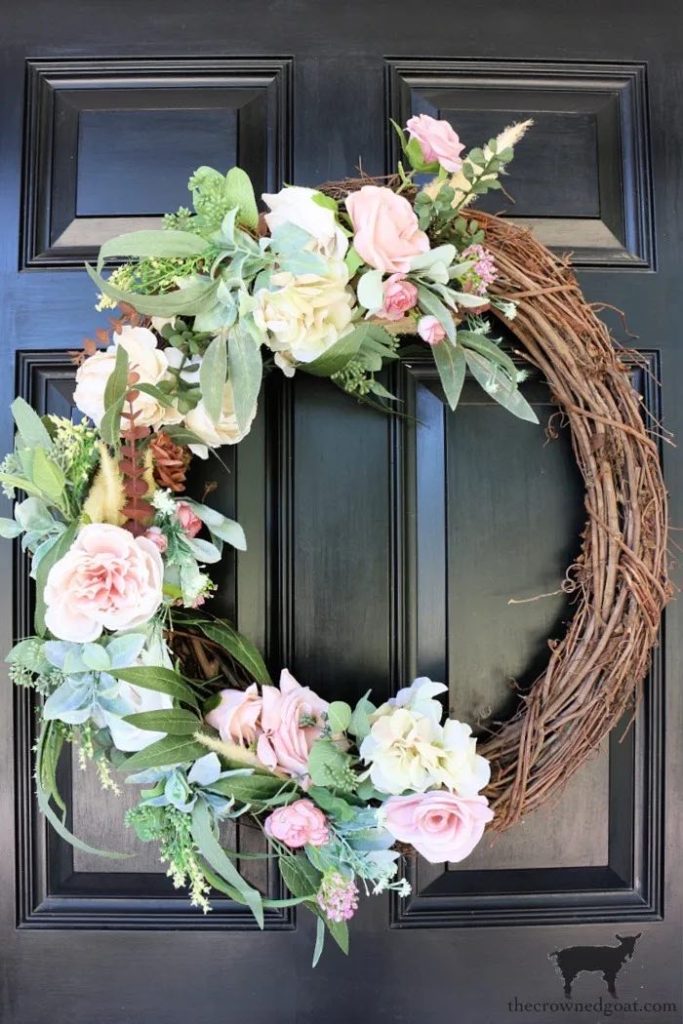 grapevine wreath covered in flowers on one side hanging on a black door