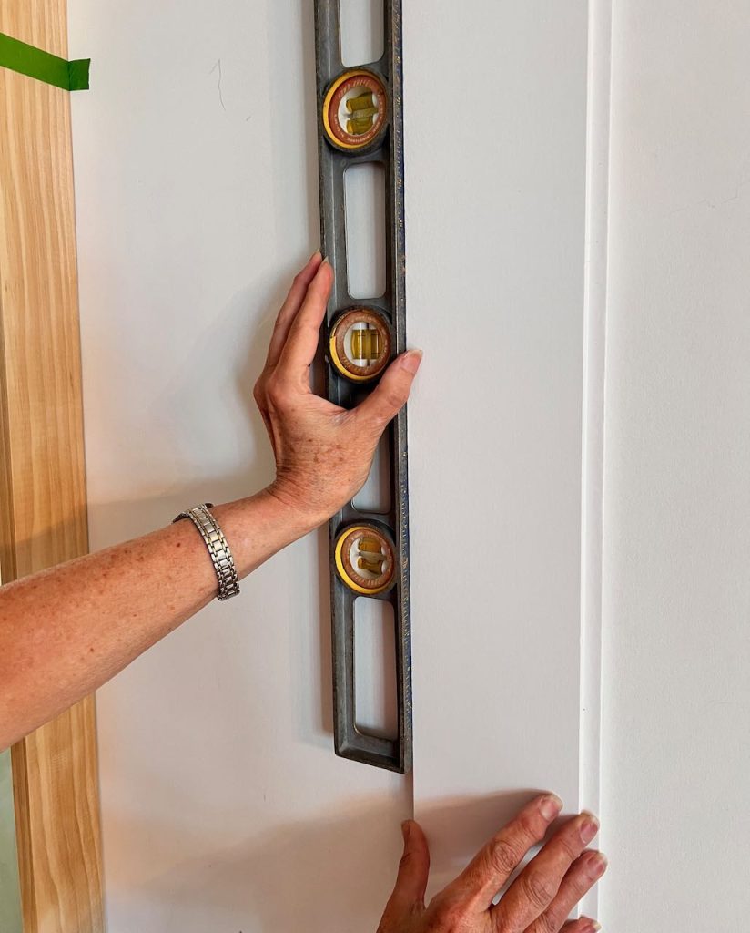 woman's hand holding a long level against a piece of shiplap on the wall