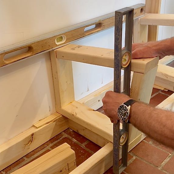 man's hands holding a level vertically against a bench frame