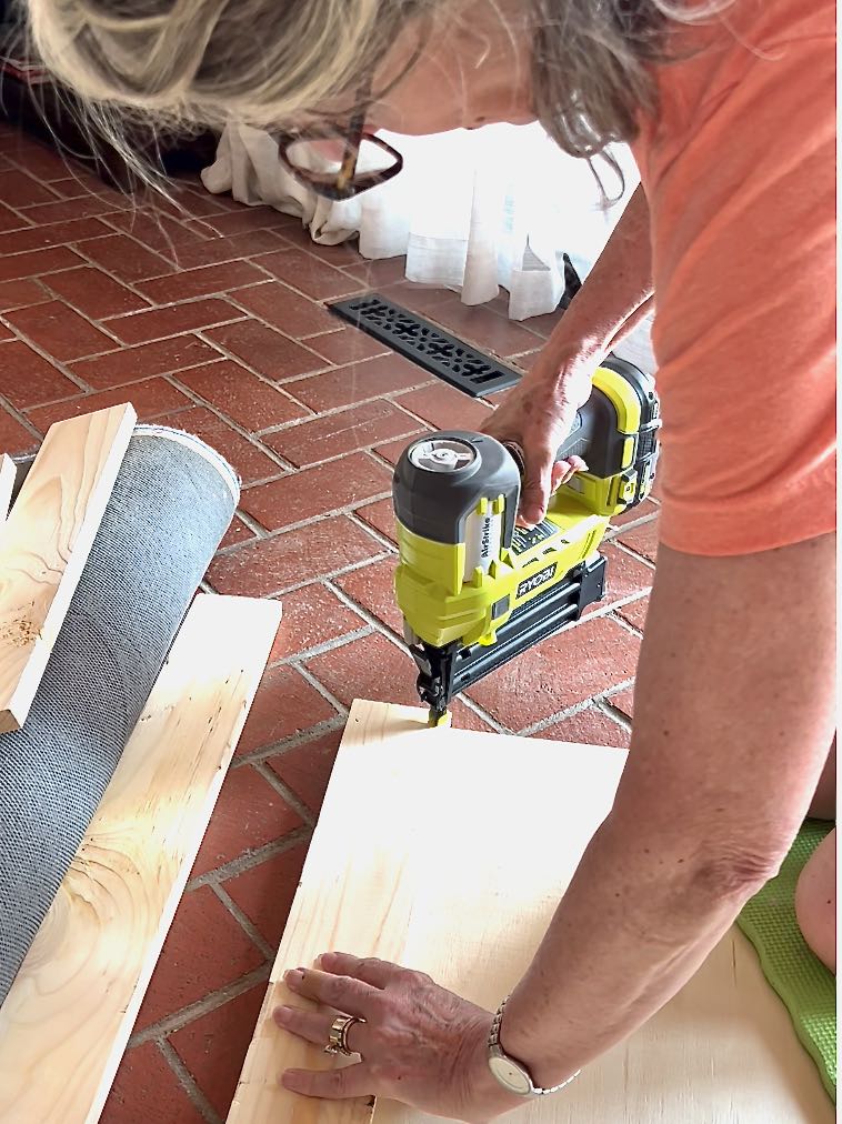 woman kneeling on the backer board with a brad nailer attaching the frame to the backer