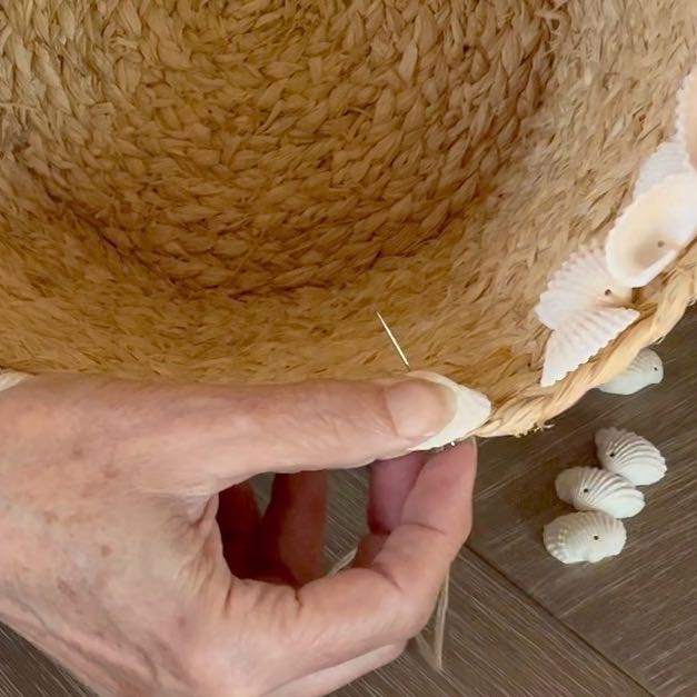 super closeup of a needle coming up through a basket on one side of a shell being held in place by a woman's thumb