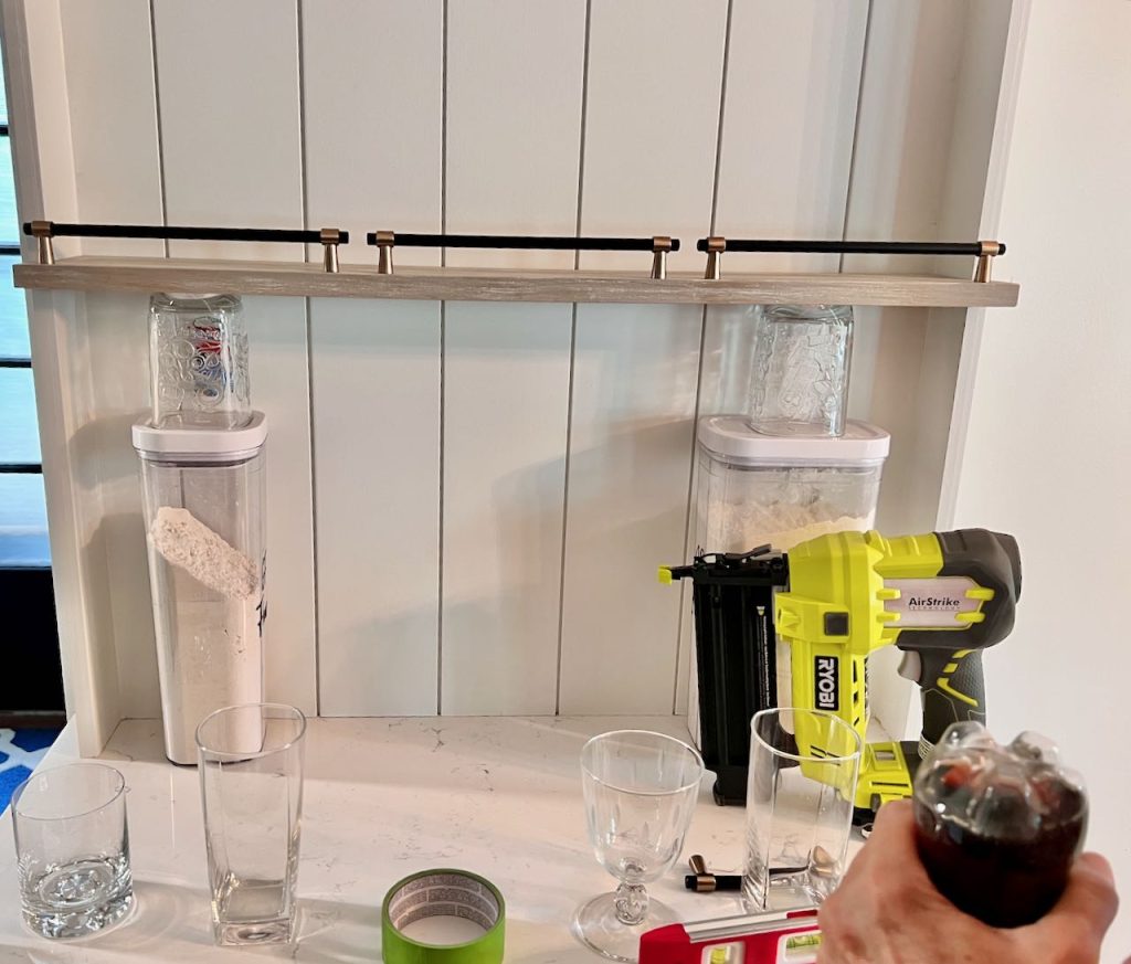 One shelf propped on canisters and glasses with an assortment of glasses on the counter