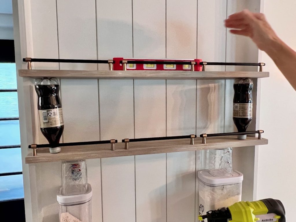 woman's hand is setting a level on an open shelf propped on two soda bottles