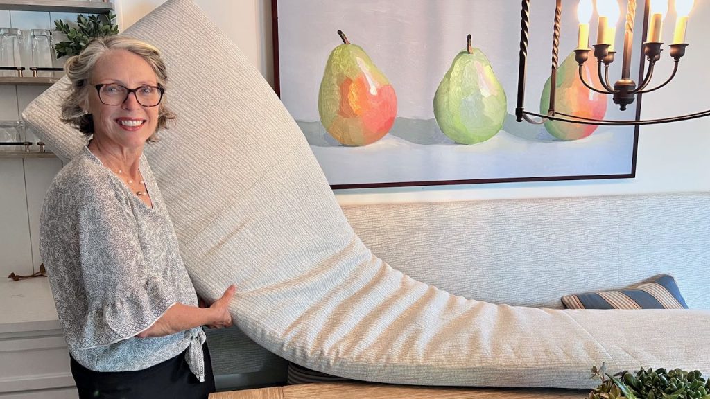 Woman holding one end of a very long cushion that drapes across and off the picture