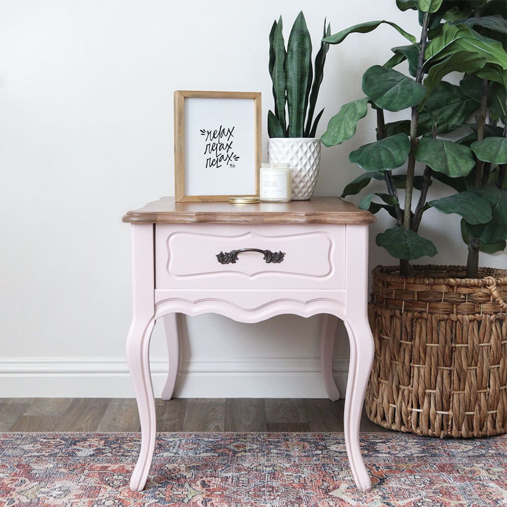 a sweet nightstand with a refinished wood top and a soft pale pink bog and legs next to some house plants