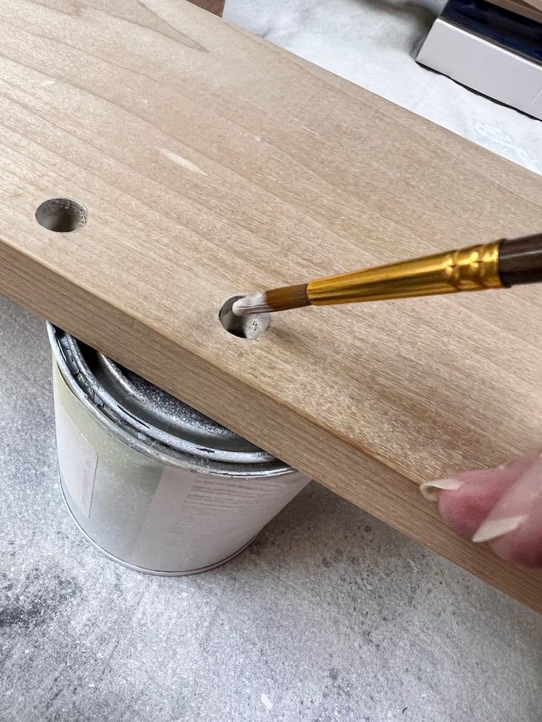 closeup of the tip of an artist paint brush painting inside drilled holes