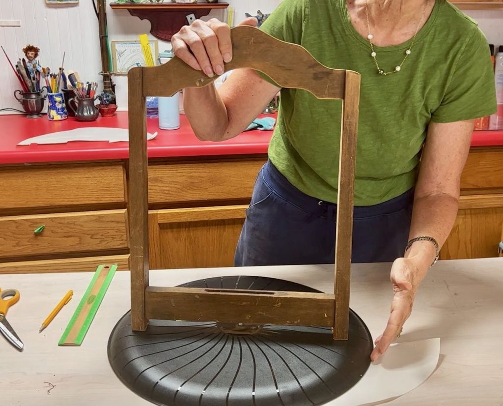 back of a vintage chair is held standing on a large plastic tray to test the size