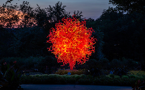 huge blown glass sculpture is lit at night in an outdoor garden setting