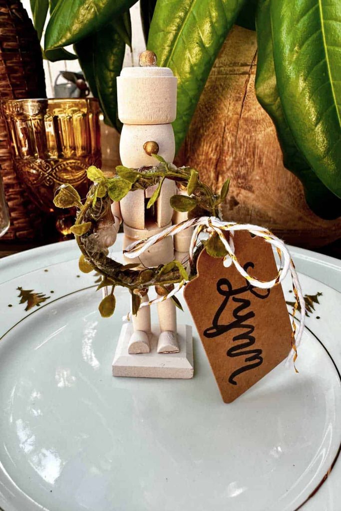 a small nutcracker holding wreath and a nametag is standing on a Christmas dinner plate