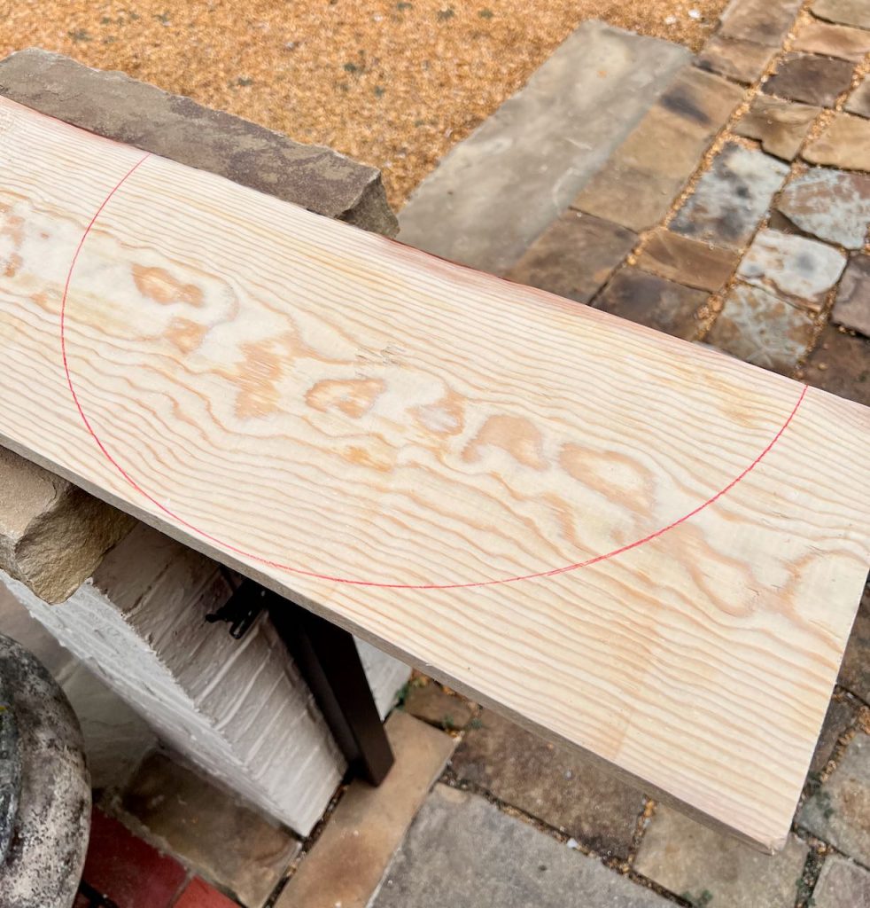 a piece of pine is resting on a stone post with a red semi circle drawn on it for cutting