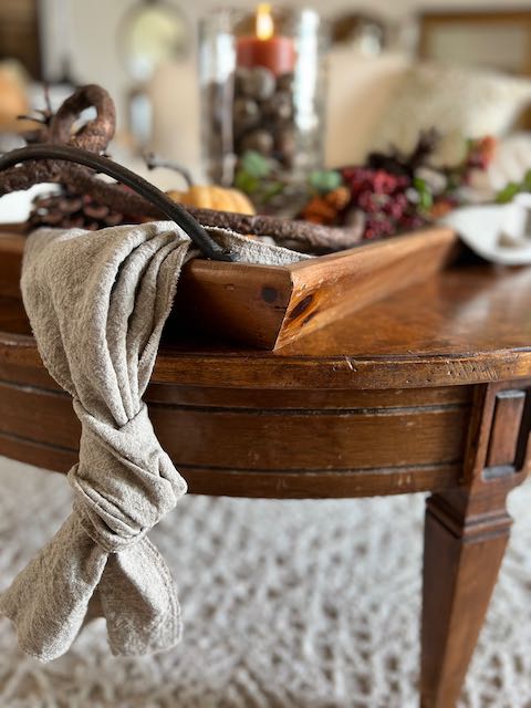 a linen table runner is knotted at the end and threaded through the handle of a wood tray