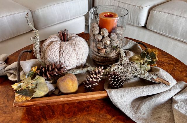 Neutrall colored pumpkins applle and branch with a pillar candle in a hurricane glass