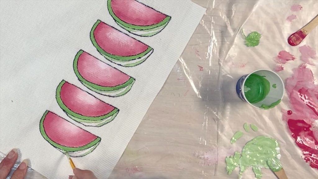 woman holding a paint brush and painting the rind of the watermelon