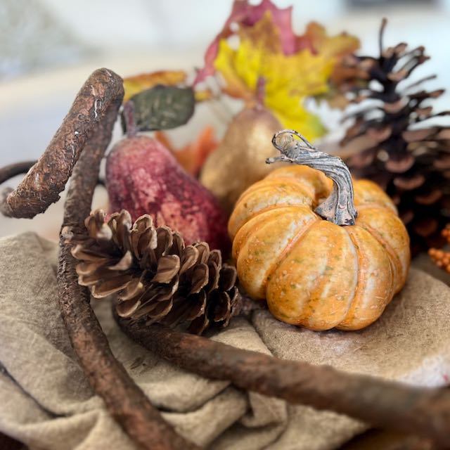 closeup of one corner of a Fall floral arrangemnt featuring a pinecone, pumpkin and pear