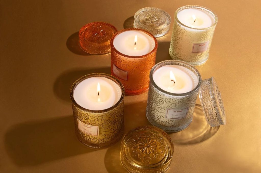 Four Candles in different colored decorative glass jars are lit 