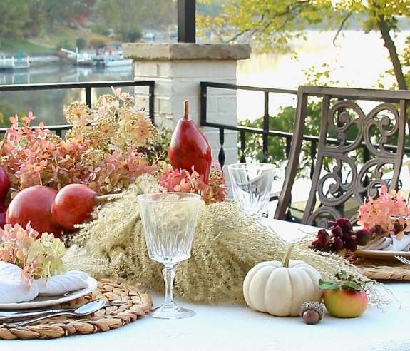 Fall table set with dried grasses and gourds and hydrangeas on patio overlooking lake at sunrise