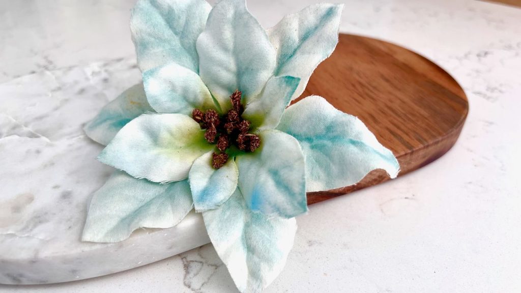 closeup of a finished faux poinsettia flower accented with deep blue-green watercolor paints resting on a wood and marble cutting board