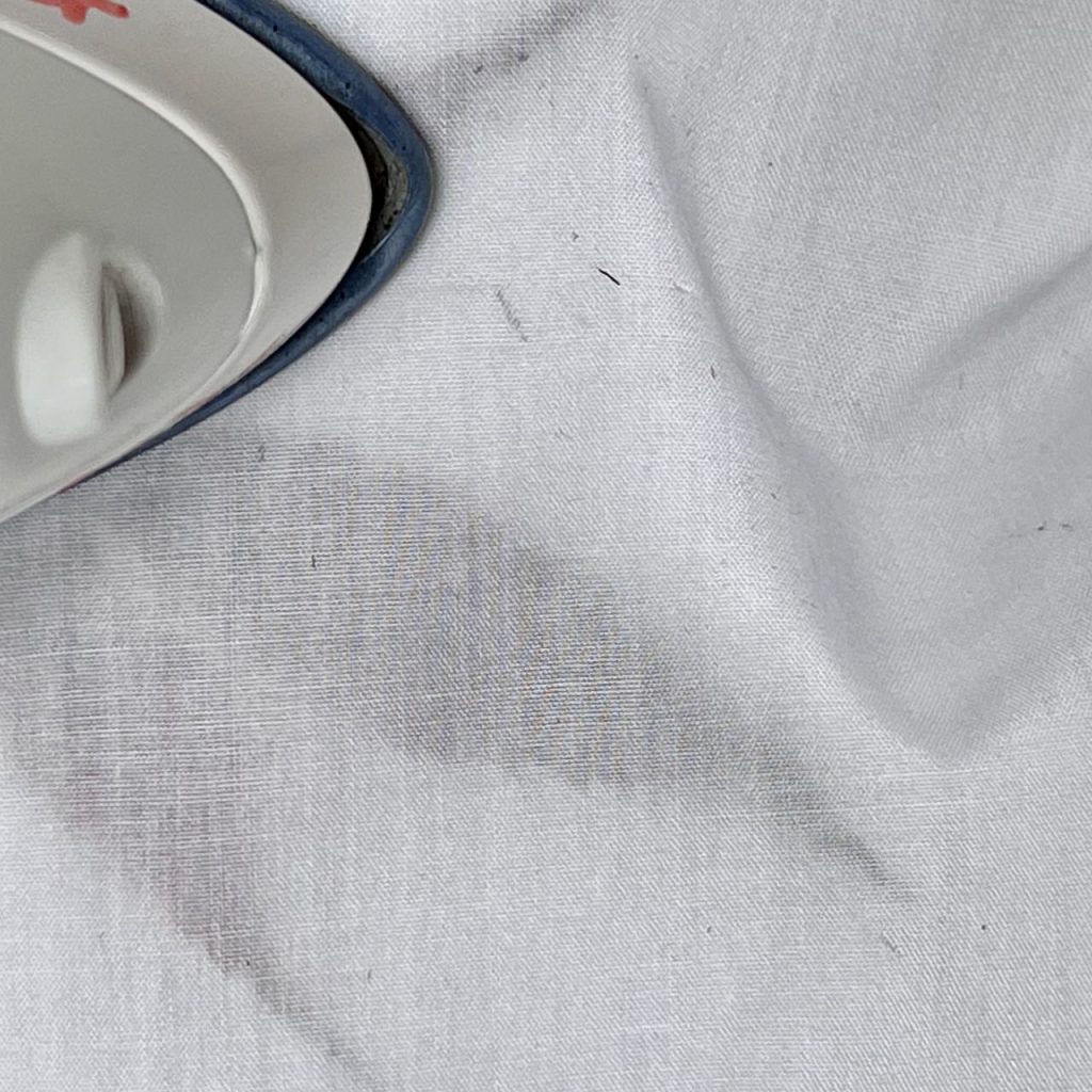 the tip of an iron is seen ironing a thin cotton fabric over a preserved leaf