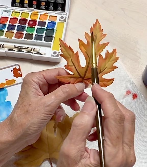 closeup of a woman painting watercolors along the edges of a faux leaf to give it more color