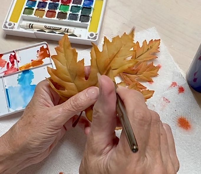 closeup of a woman adding color to an artificial Fall leaf using watercolors