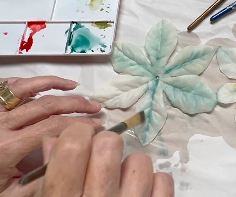 closeup of a woman adding color to the petals of a faux flower using watercolor paints