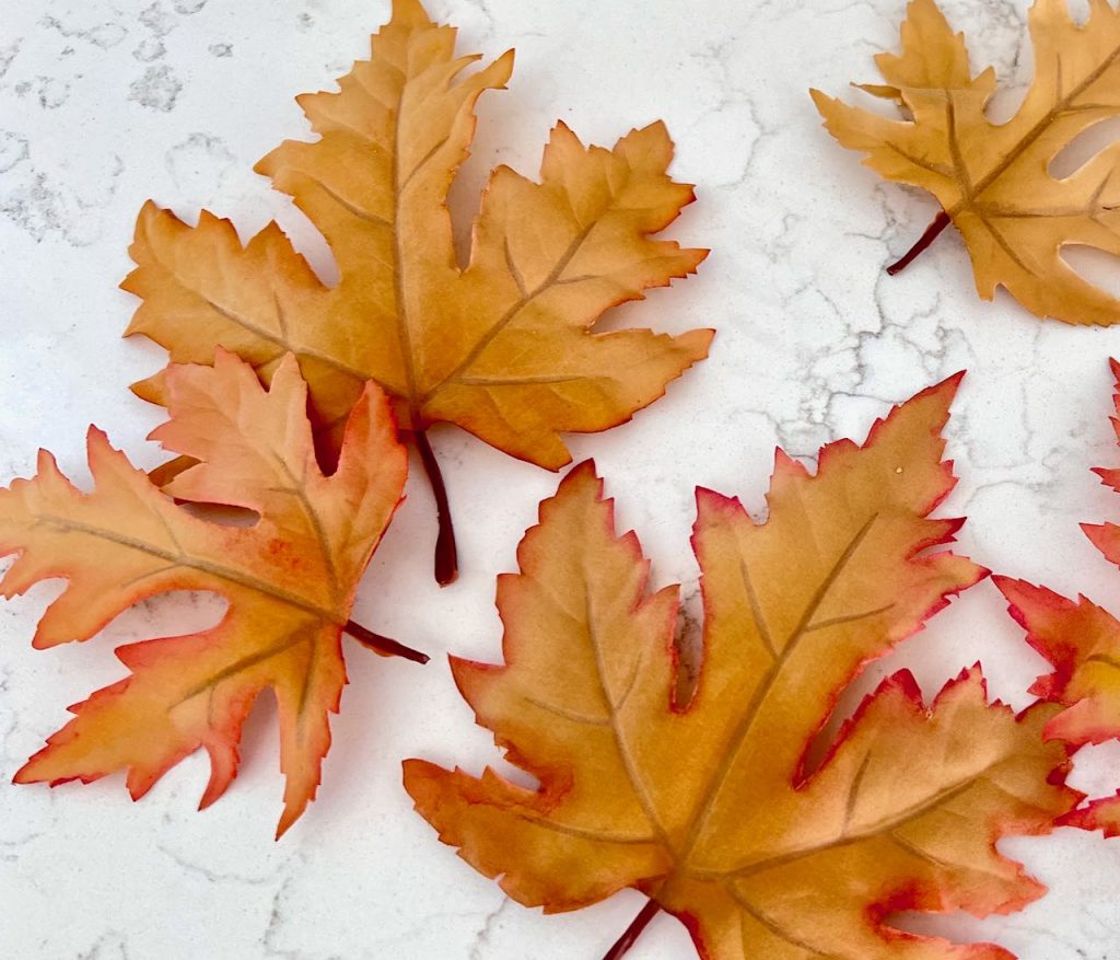 faux leaves with painted edges in bright Fall colors laying on a quartz counter