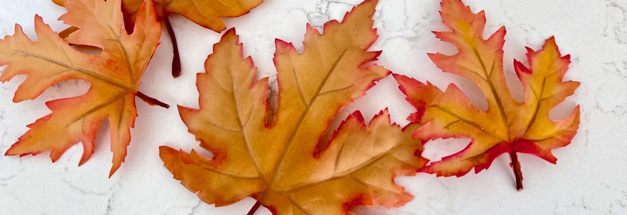 faux leaves with painted edges in bright Fall colors laying on a quartz counter