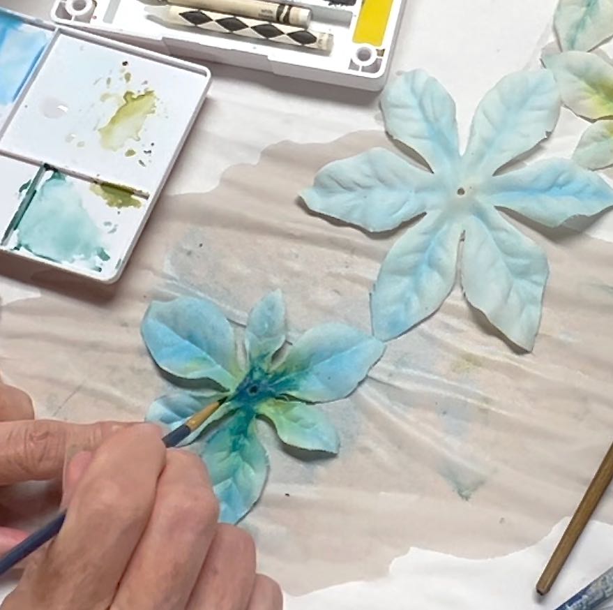 closeup of a woman adding dark watercolor paint to the center of of a silk flower