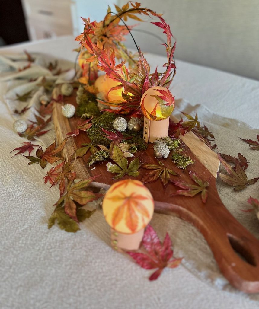 view off tablescape dpwn length of table with candlle in large garden orb and three small glowing orbs and preserved Fall leaves