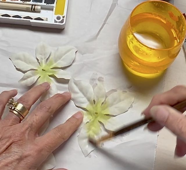 woman's fingers holding silk flower petals while brushing them with water