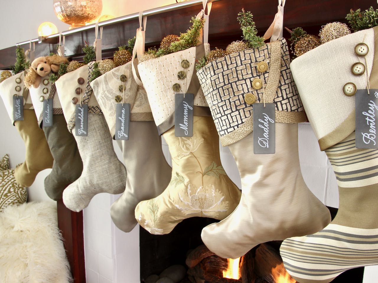 7 coordinating yet unique Christmas stockings are hagning from a mantel above a fire. Sea glass name tags hang from the top of three buttons on each cuff