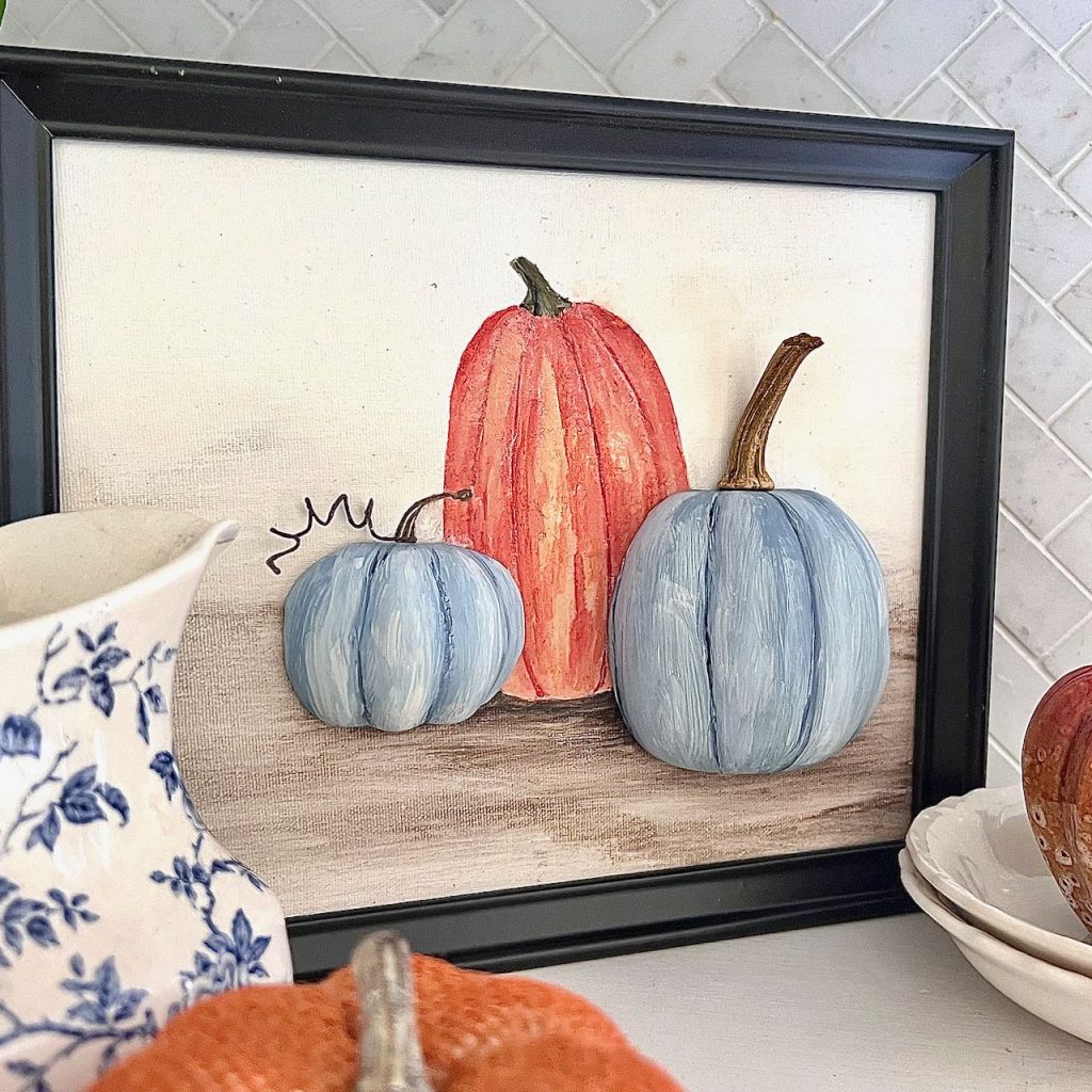 blue and orange 3D pumpkin wall art in a black frame sitting on a kitchen open shelf