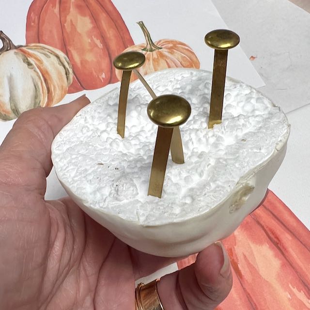 closeup of 3 large brads stuck into the styrofoam cut side of a faux pumpkin