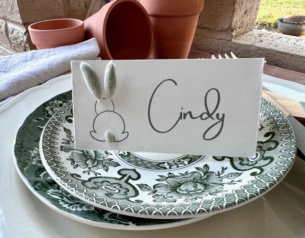 closeup of a place card on a transferware plate with the outline of thhe back of a bunny with fresh lambs ear for the ears and fuzzy tail.