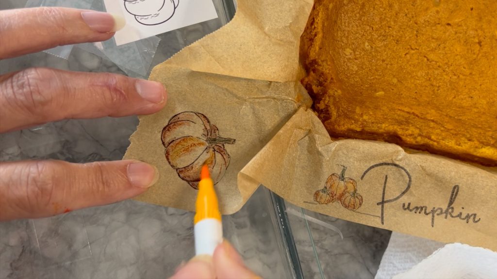 fingers holding the parchment paper and a marker is coloring in the pumpkin outlines