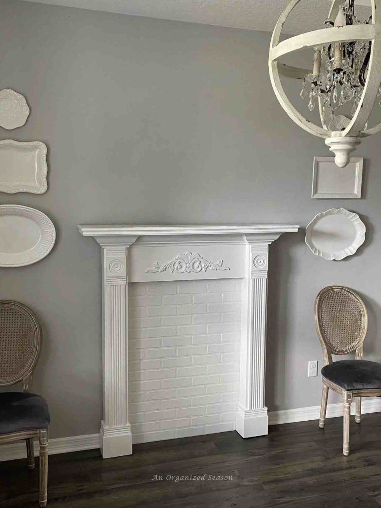 A faux mantel is installed on wall  with a chair on each side
