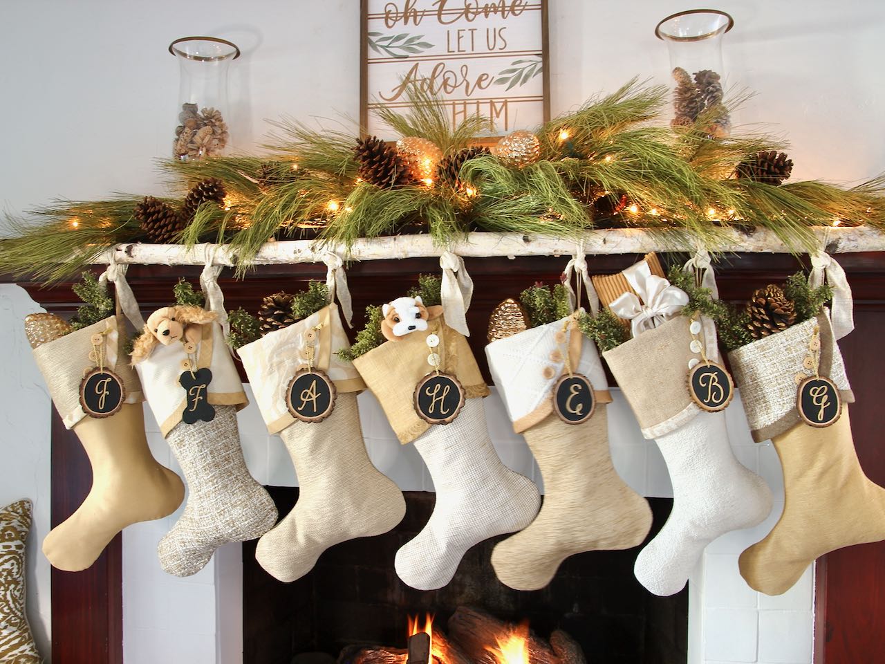 7 coordinating yet unique Christmas stockings hang from a birch branch on a mantel. Tree slice name tags hang from the cuffs' buttons