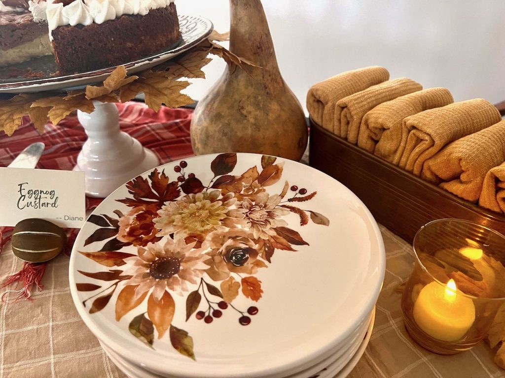 stack of pretty Fall dessert plates next to a brass box holding napkins